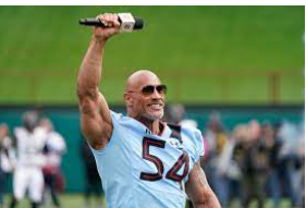 Dwayne Johnson holds up microphone at the XFL game.