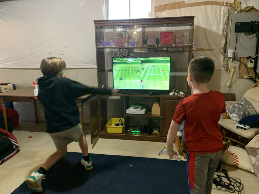 Two young boys face off in Wii Tennis downstairs on a basement TV.
