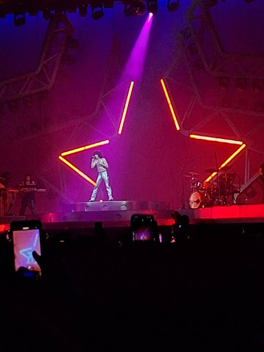 Conan Gray performs on stage with a bright neon star in the background